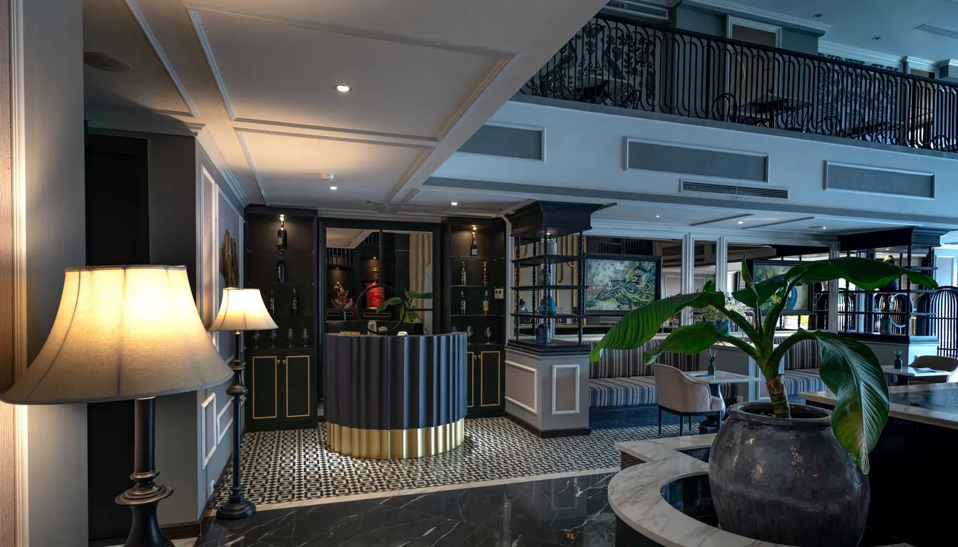 An elegant hotel lobby with a curved reception desk, marble floor, floor lamps and a large potted plant.
