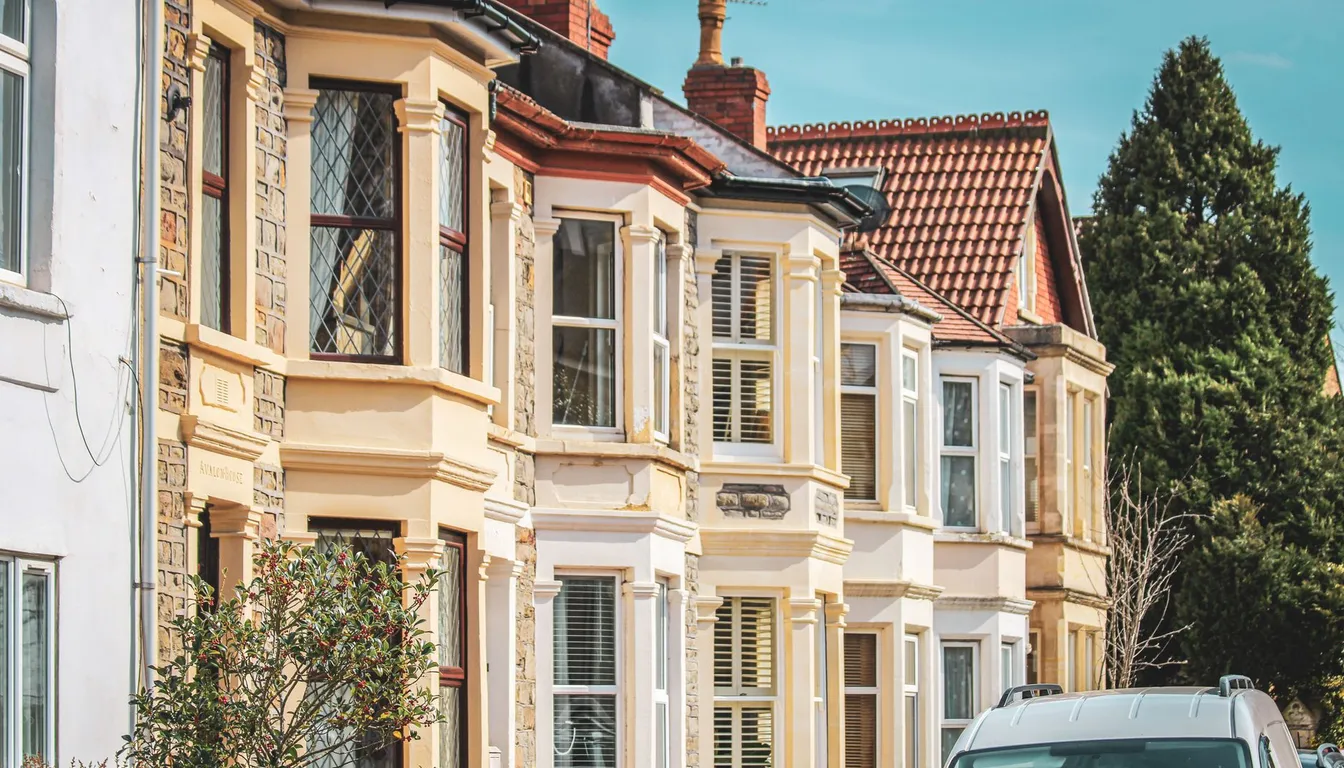 A row of British terraced houses with cream bay windows and red tiled roofs, with a white van parked on the street in front.